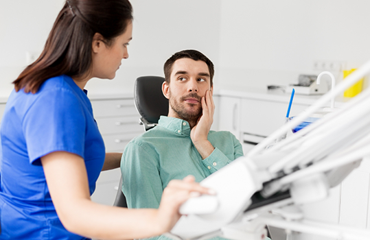 Man sitting in dental chair with tooth pain and looking at dentist