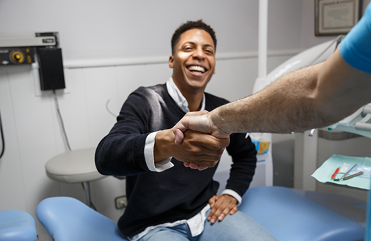 Man in dental chair shaking dentists hand