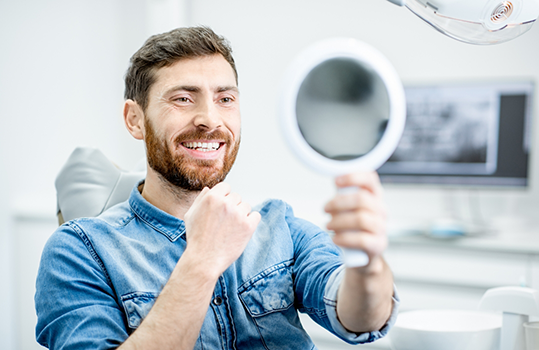Male dental patient checking smile in handheld mirror