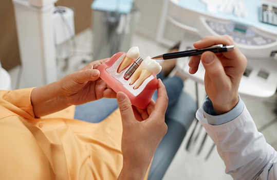 Man sitting in dental chair holding a dental implant model