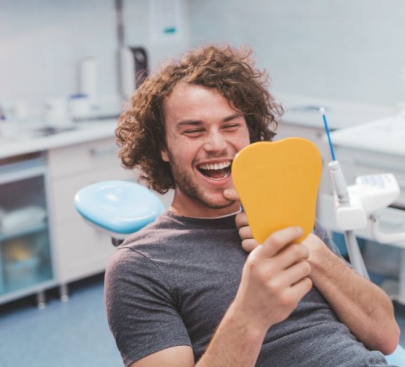 Man sitting in dental chair and checking smile in mirror
