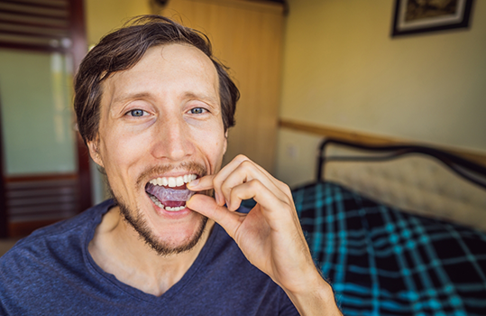 Man standing in front of bed putting in nightguard