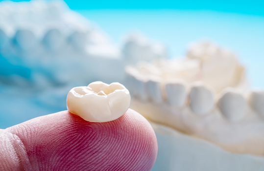 Close up of finger holding crown for restorative dentistry in Montague
