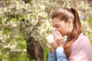 Woman blowing nose suffering from allergies outdoors. 