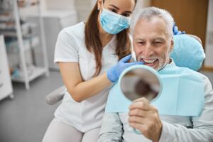 Dentist touching teeth of man with white hair in dental chair